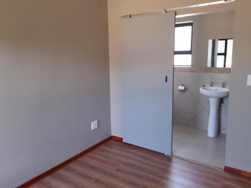 Empty bedroom featuring laminate flooring and a sliding barn door leading to an en-suite bathroom with a pedestal basin and tiled finishes.