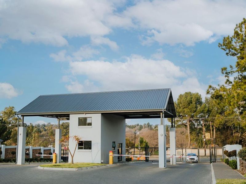 A secure gated entrance to the apartment complex featuring a modern gatehouse, boom gate access control, and paved driveway.