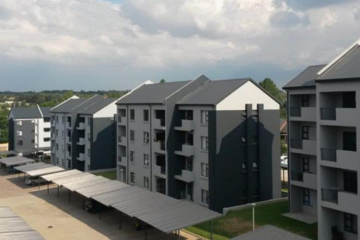 Aerial view of a modern apartment complex featuring multi-story residential buildings, covered parking structures, and paved access areas.
