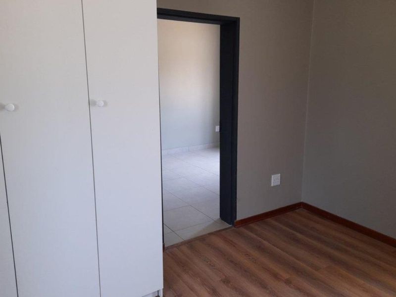 An empty bedroom featuring laminate flooring, built-in cupboards, and a doorway leading to an adjacent tiled room.