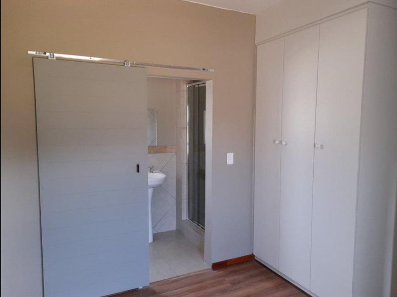 A clean bedroom featuring laminate flooring, a large built-in wardrobe, and a sliding barn door providing access to an en-suite bathroom.