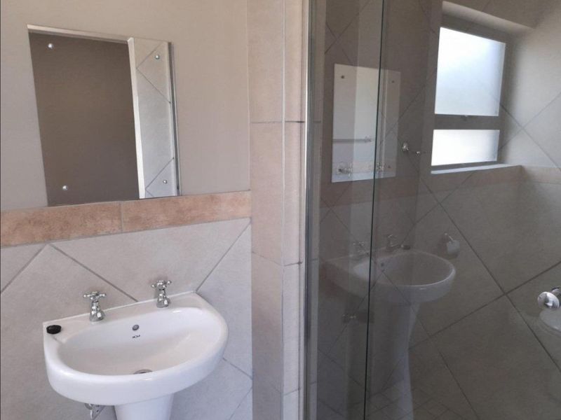 A clean, functional bathroom featuring a pedestal basin, a glass-enclosed shower, and neutral wall tiling with a frosted window for natural light.