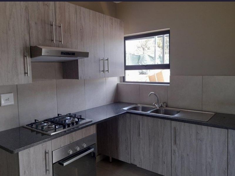 Modern kitchen featuring light wood-grain cabinetry, dark laminate countertops, a gas hob, built-in oven, and a stainless steel double sink.