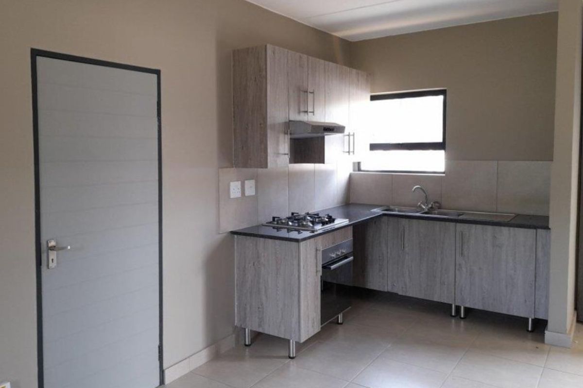 A clean, modern kitchen featuring wood-look cabinetry, a gas hob, built-in oven, extractor fan, and neutral tiled flooring.