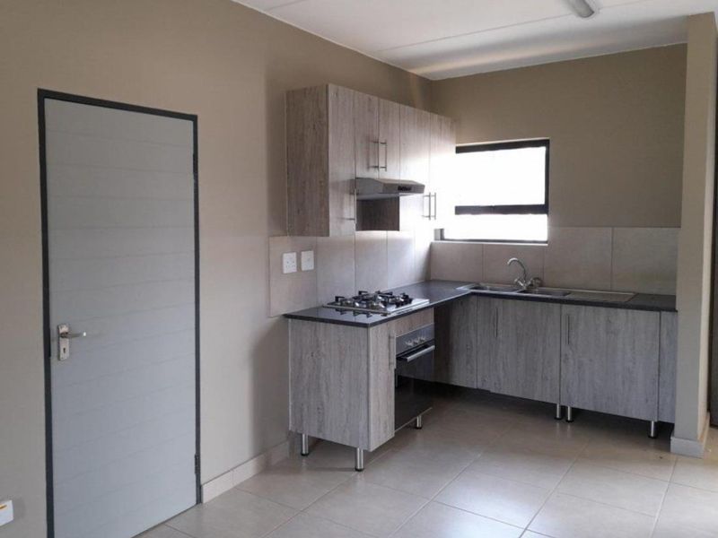 A clean, modern kitchen featuring wood-look cabinetry, a gas hob, built-in oven, extractor fan, and neutral tiled flooring.