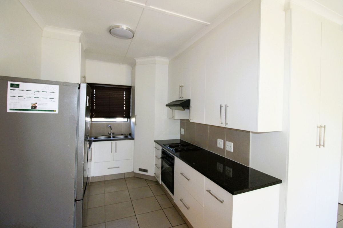 A clean, modern kitchen featuring white cabinetry, dark granite countertops, built-in oven, hob, extractor fan, and tiled flooring.