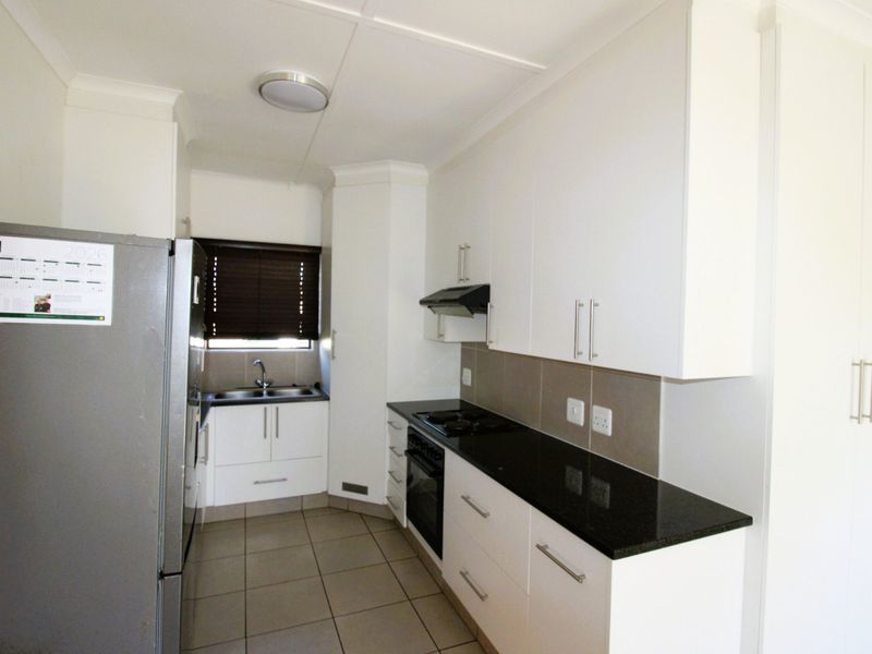 A clean, modern kitchen featuring white cabinetry, dark granite countertops, built-in oven, hob, extractor fan, and tiled flooring.