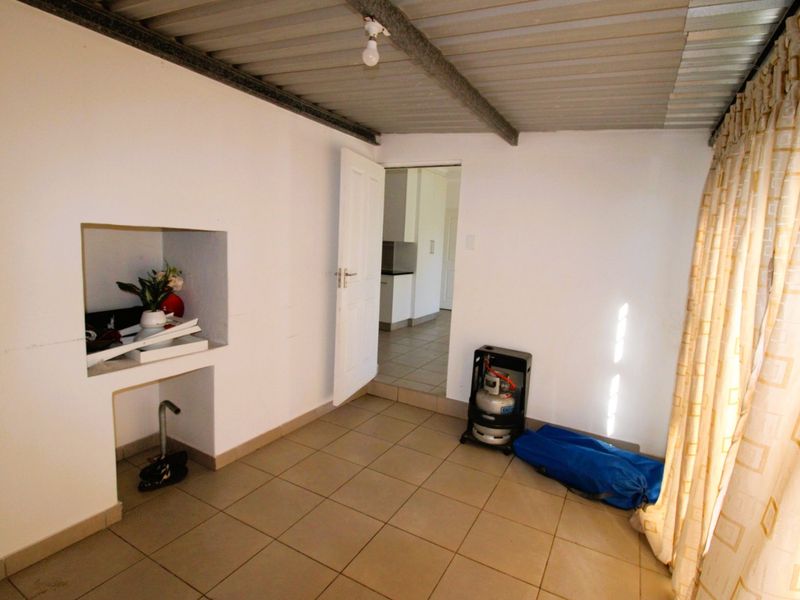 A functional utility space featuring tiled flooring, an exposed corrugated metal ceiling, and a built-in wall niche, providing versatile storage or workspace potential.