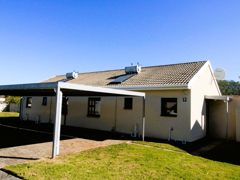 Front view of the property featuring a paved driveway, carport, and roof-mounted solar water heating system.