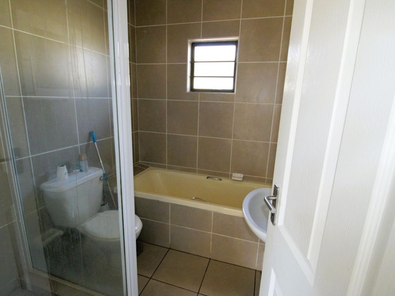 A functional bathroom featuring a shower enclosure, bathtub, toilet, and pedestal basin with neutral wall and floor tiling.