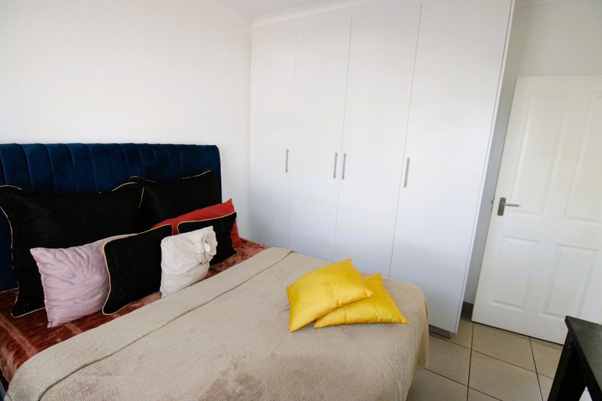 A bedroom featuring neutral tiled flooring and white built-in cupboards providing ample storage space.
