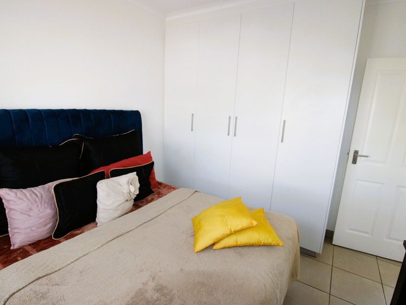 A bedroom featuring neutral tiled flooring and white built-in cupboards providing ample storage space.
