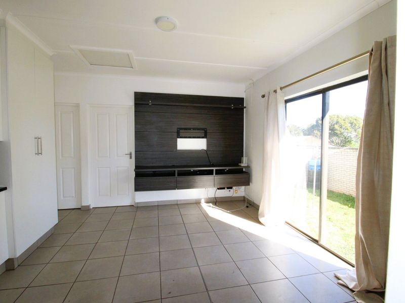 A bright, open-plan living area featuring neutral tiled flooring, a modern built-in media console, and large sliding glass doors providing access to the garden.