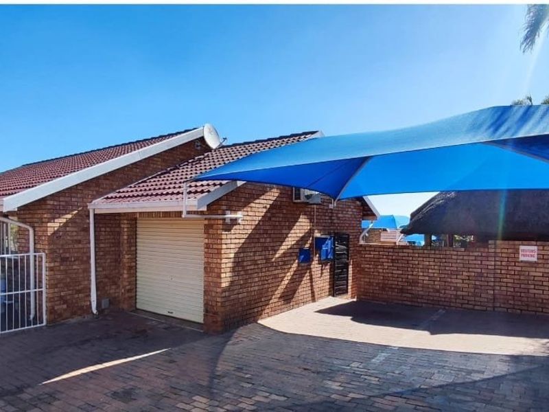 Exterior view of a brick house featuring a garage, paved driveway, and a blue shade sail covering the parking area.