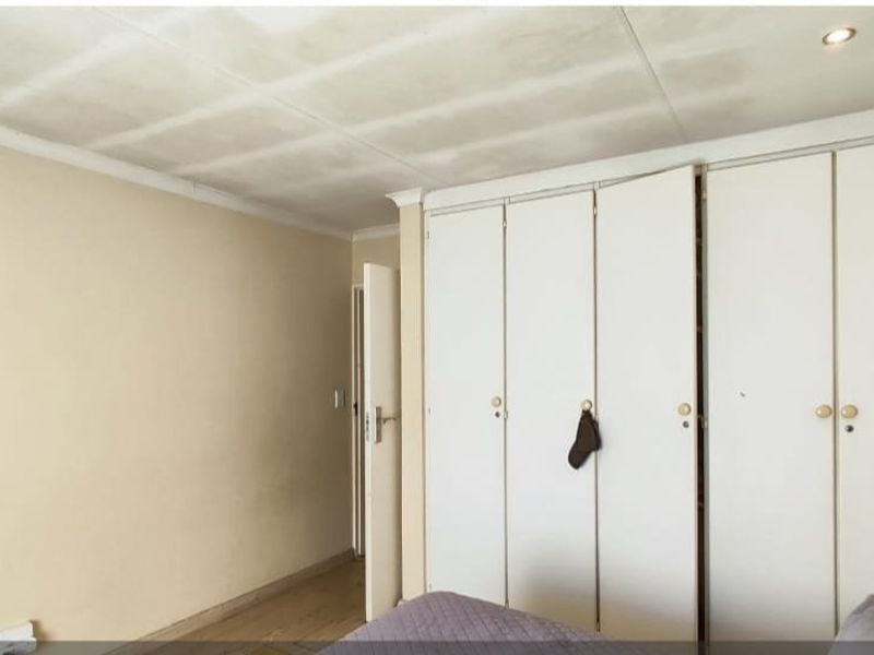A bedroom featuring built-in cupboards and recessed ceiling lighting, requiring cosmetic updates to the walls and ceiling finishes.