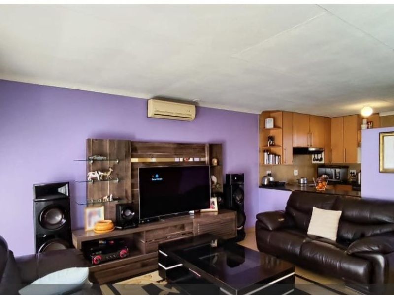 Open-plan living area featuring a kitchen with built-in cabinetry and a lounge space equipped with a wall-mounted air conditioning unit.