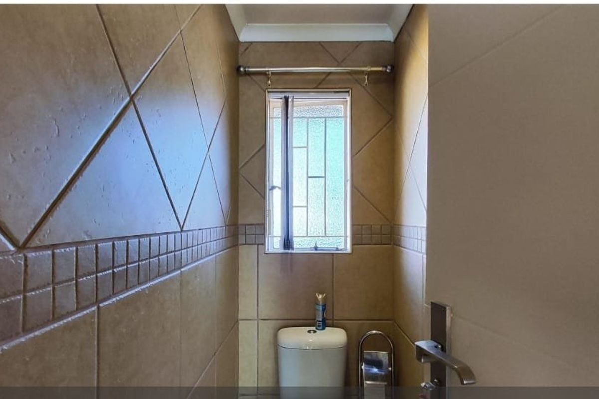 A compact bathroom featuring full-height ceramic wall tiles and a window with security bars.