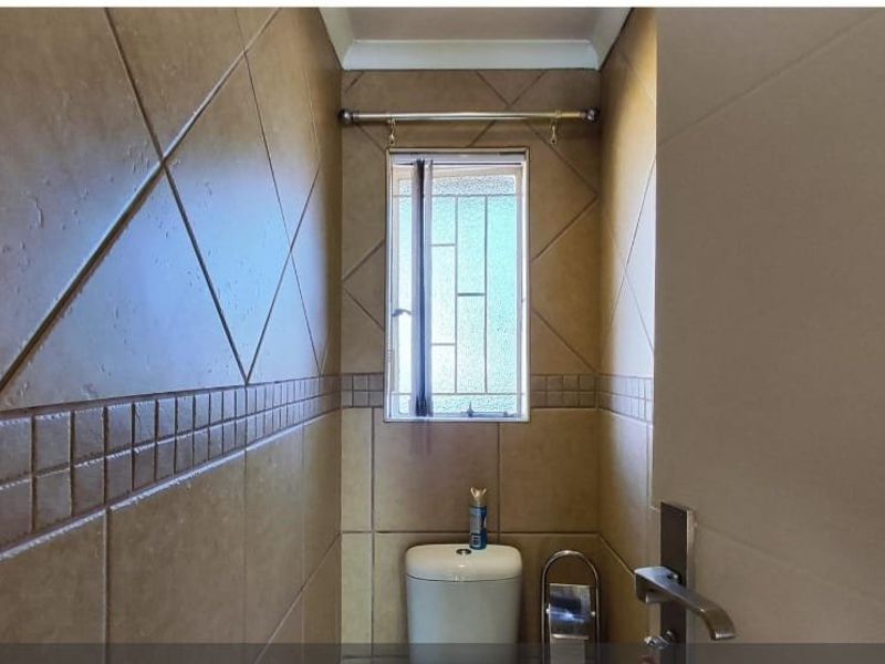 A compact bathroom featuring full-height ceramic wall tiles and a window with security bars.