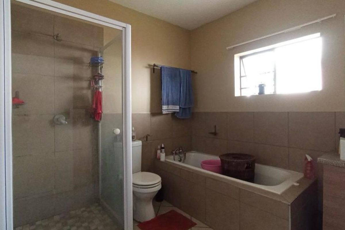 A functional bathroom featuring a separate shower enclosure, bathtub, toilet, and a vanity cabinet with a basin, finished with neutral wall and floor tiles.