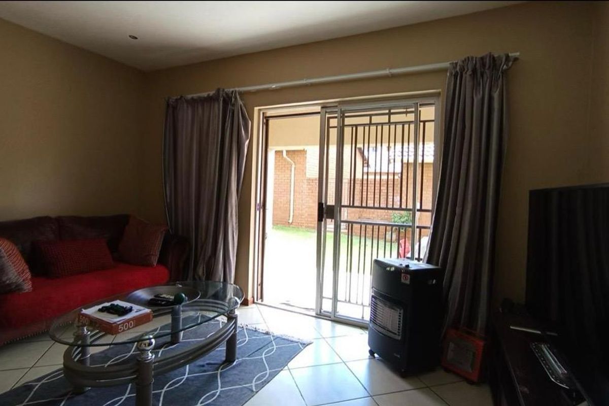 A living room featuring tiled flooring and a sliding glass door with a security gate, providing direct access to the rear patio and garden.