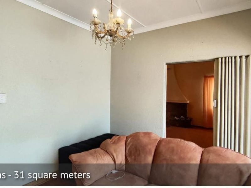 A living room featuring a classic chandelier, coving, and a folding door leading to an adjacent space.