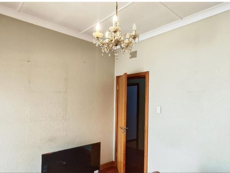 An empty living room featuring a classic chandelier, coved ceiling, and timber door frame, awaiting cosmetic updates to refresh the wall finishes.