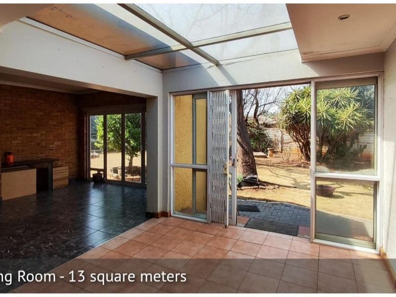 Open plan living area featuring a skylight, tiled flooring, brick feature wall, and large sliding doors providing direct access to the rear garden.