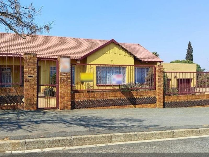 Front elevation of a single-story house featuring a tiled roof, brick boundary wall, and security fencing along the street frontage.