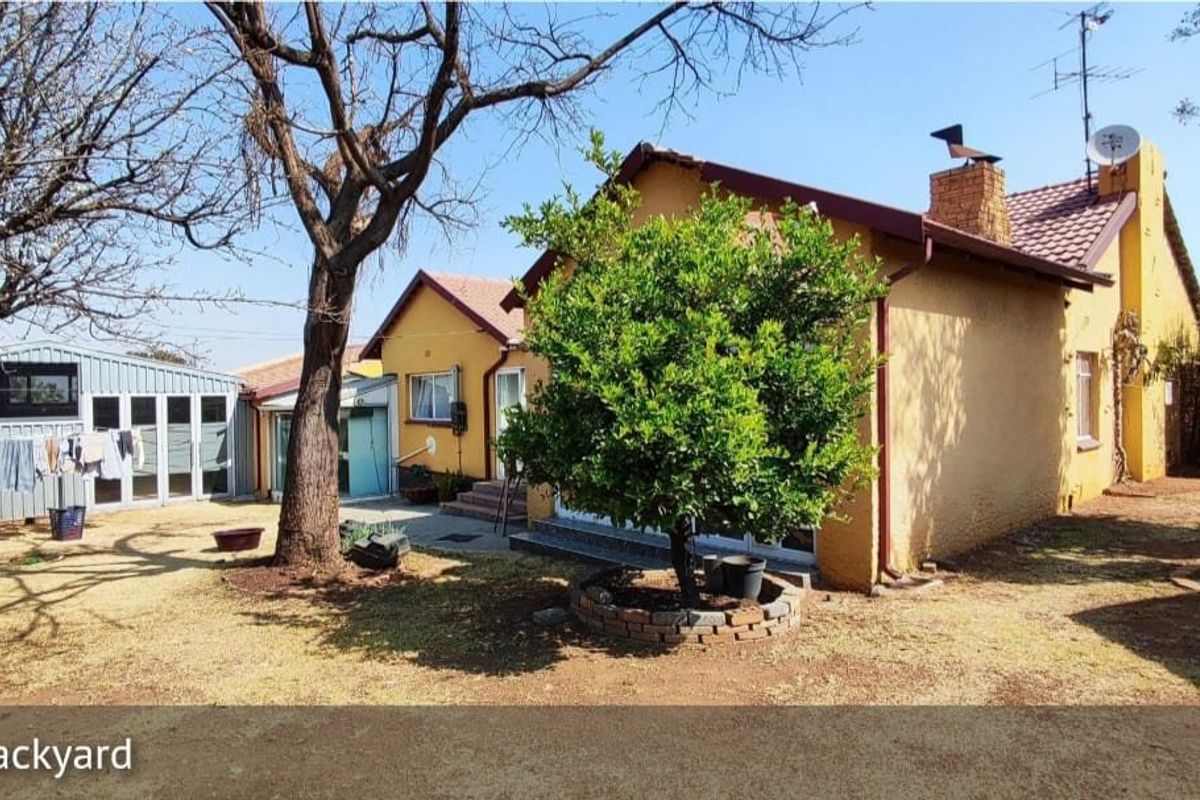 Rear view of the house featuring a tiled roof, brick chimney, and a detached metal shed set within a spacious backyard area.