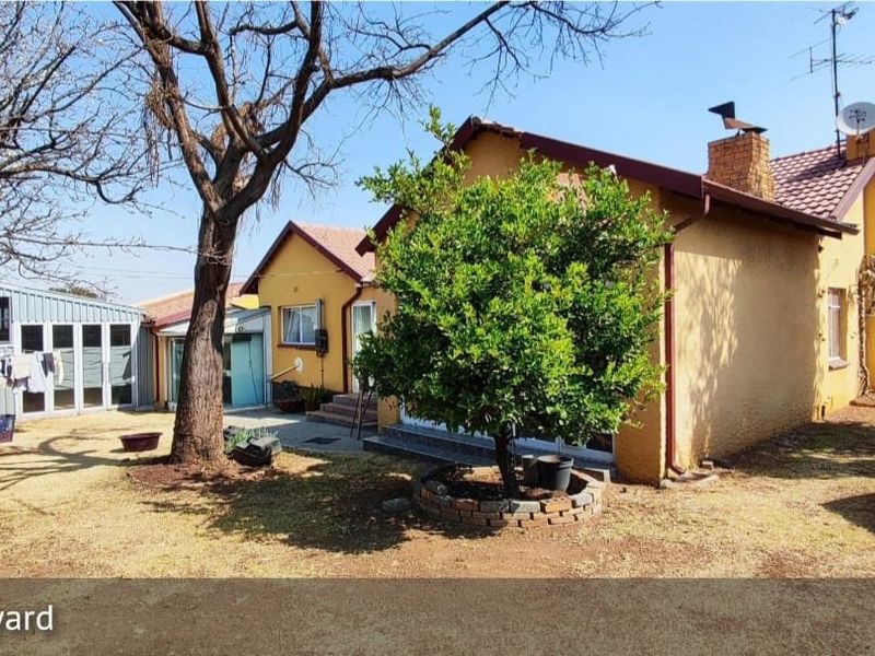 Rear view of the house featuring a tiled roof, brick chimney, and a detached metal shed set within a spacious backyard area.
