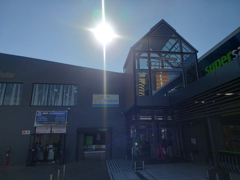 Exterior view of the commercial building entrance featuring a glass atrium and various retail signage.