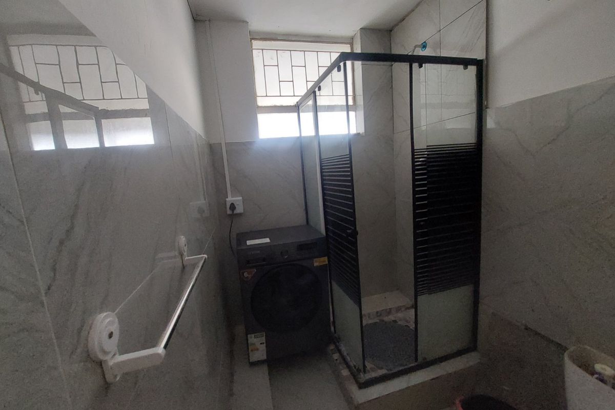 A functional bathroom featuring a glass shower enclosure, tiled wall finishes, and a window with security bars.