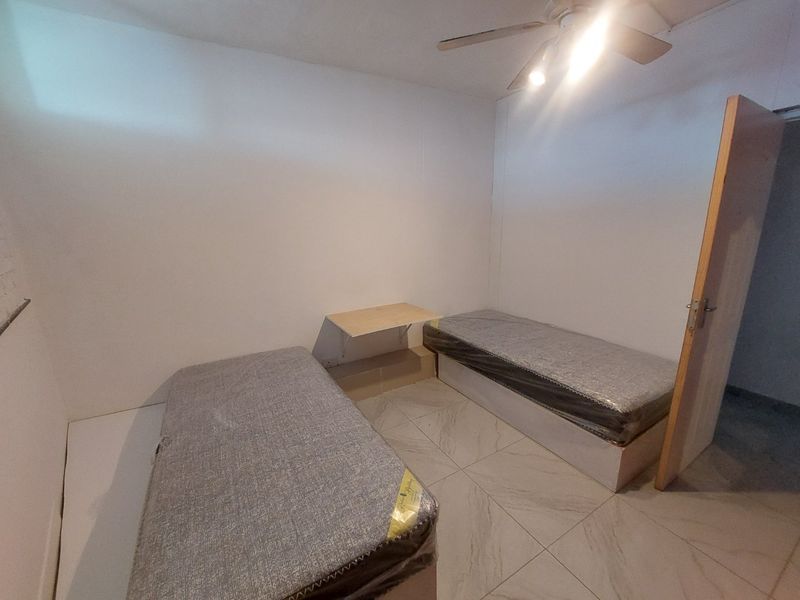 A simple bedroom featuring tiled flooring, a ceiling fan, and a built-in wall shelf, providing a functional and neutral living space.