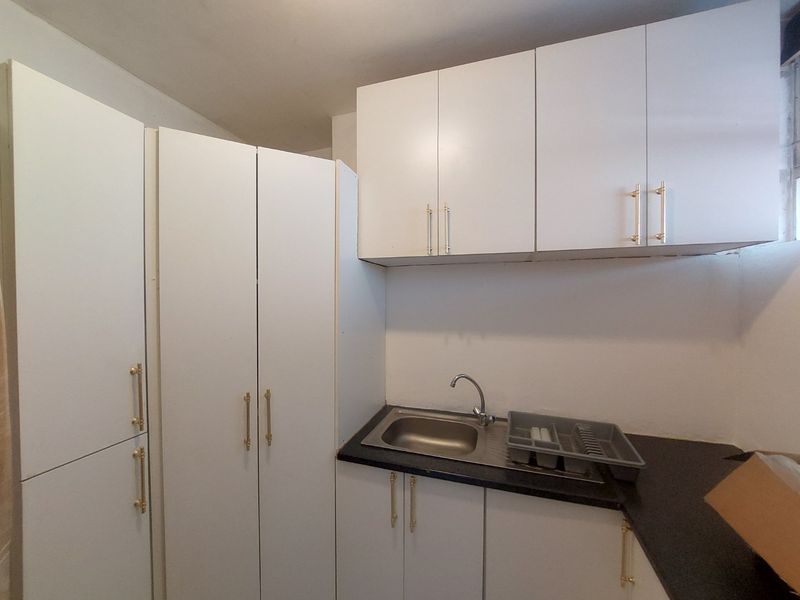 A compact kitchen area featuring white built-in cabinetry, a stainless steel sink, and dark laminate countertops.