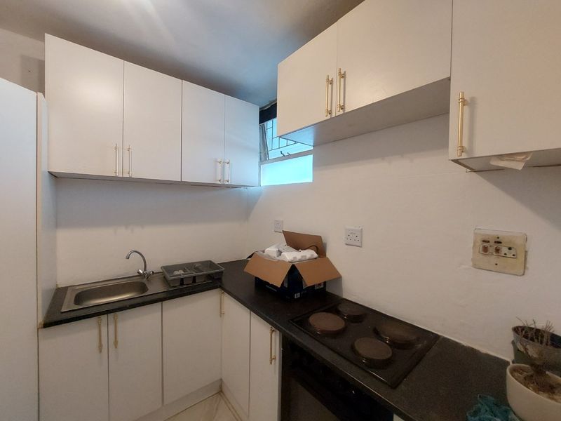 Compact kitchen featuring white cabinetry, dark laminate countertops, a stainless steel sink, and a built-in electric hob and oven.