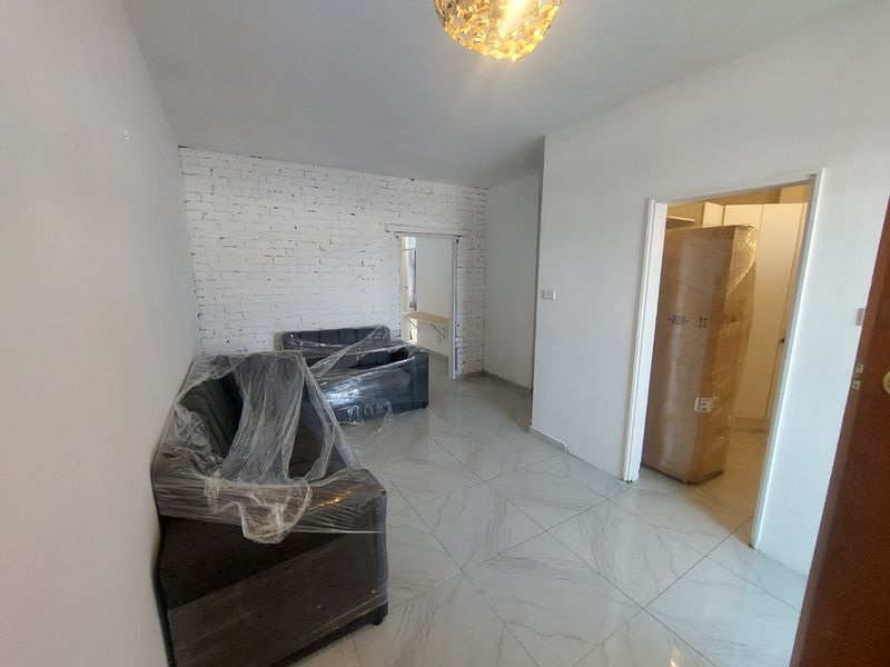 A bright living area featuring modern white porcelain tile flooring and a characterful exposed white brick feature wall.