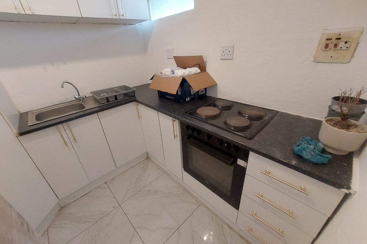Compact kitchen featuring white cabinetry, dark laminate countertops, built-in oven, electric hob, and tiled flooring.