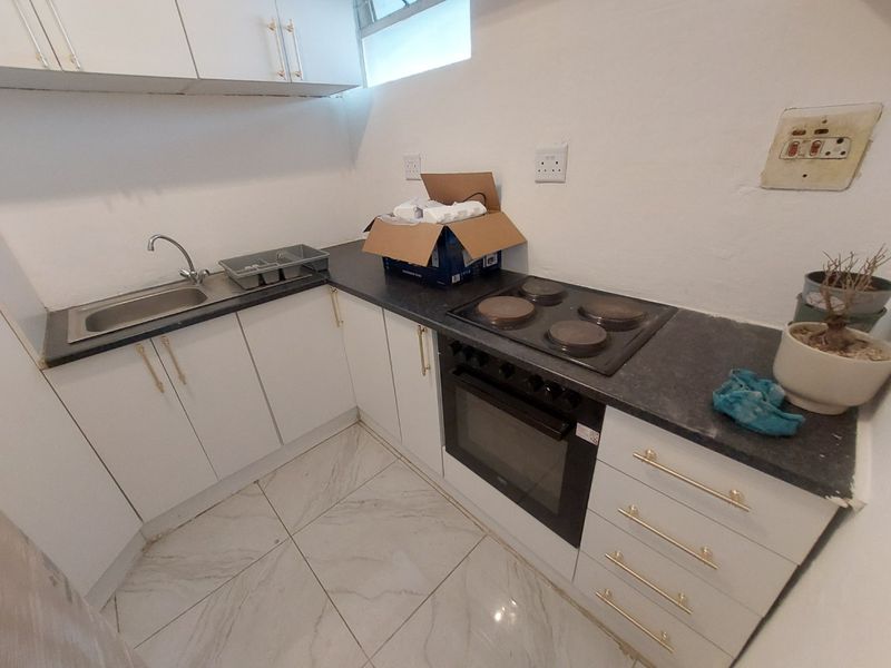 Compact kitchen featuring white cabinetry, dark laminate countertops, built-in oven, electric hob, and tiled flooring.