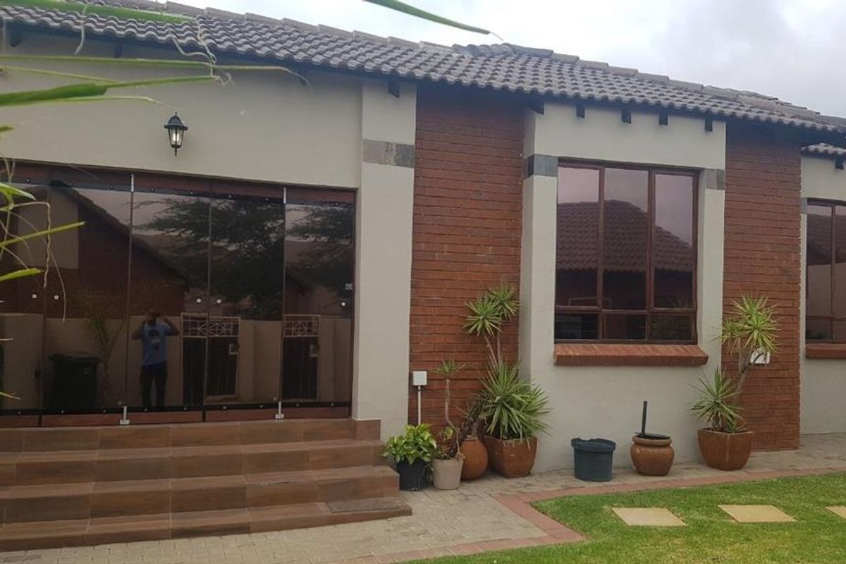 Rear view of the townhouse featuring a tiled patio, modern stacking glass doors, and a combination of brick and plastered exterior finishes.