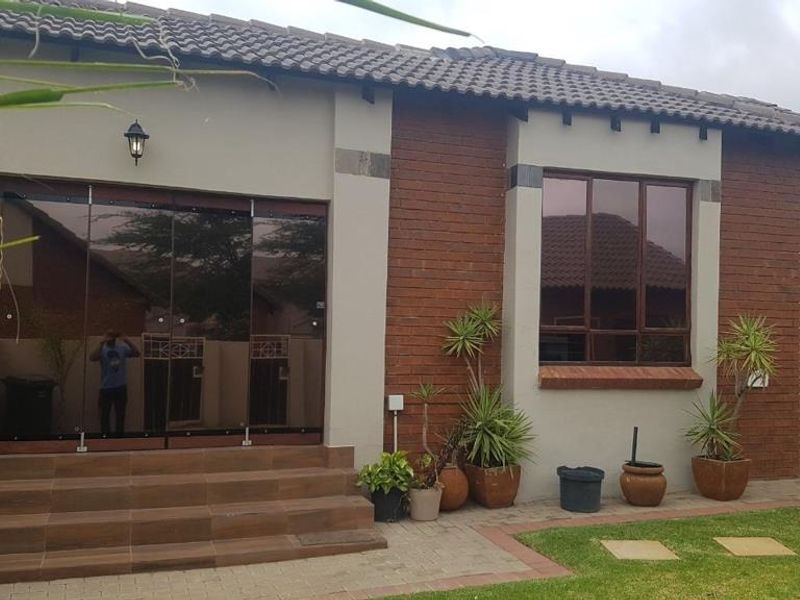 Rear view of the townhouse featuring a tiled patio, modern stacking glass doors, and a combination of brick and plastered exterior finishes.