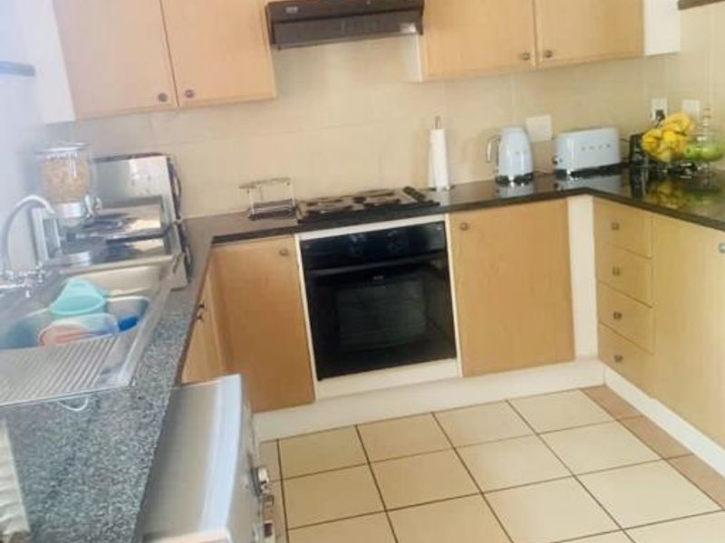 A functional kitchen featuring light wood cabinetry, granite countertops, a built-in oven with gas hob, and tiled flooring throughout.