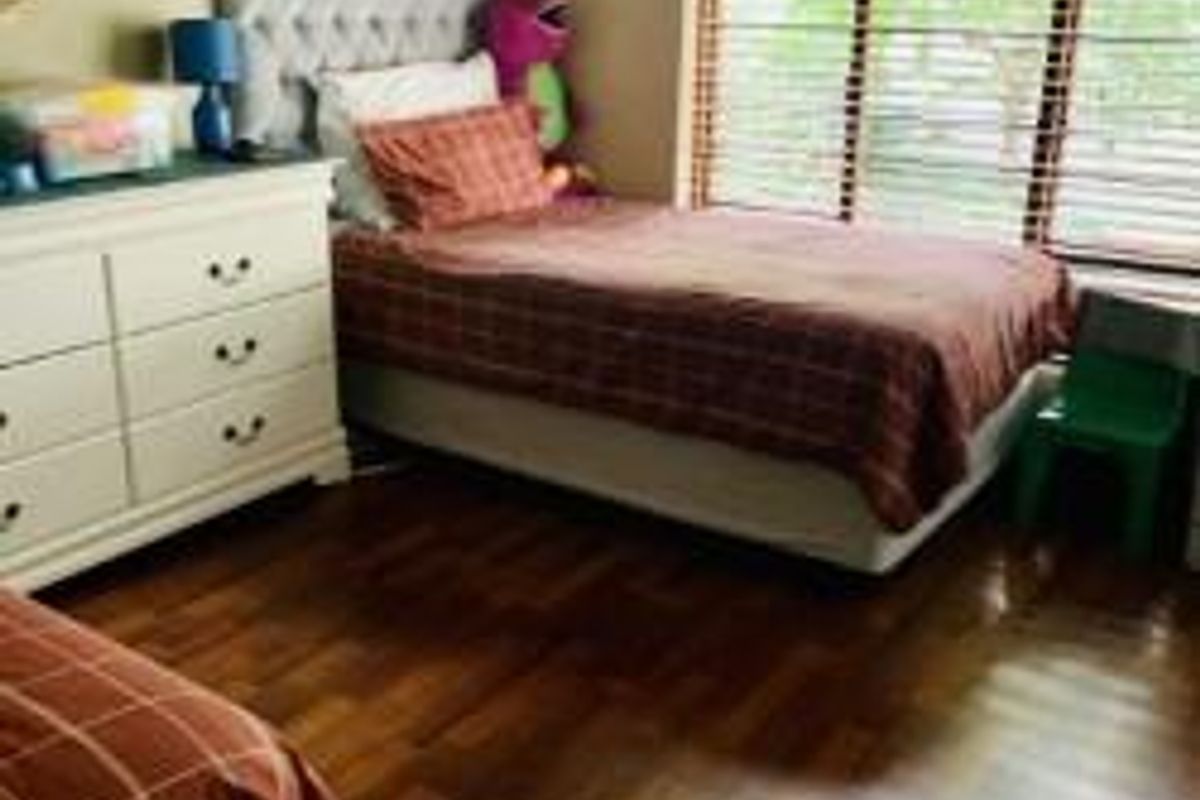 A bedroom featuring laminate flooring and venetian blinds, providing a functional space with natural light.