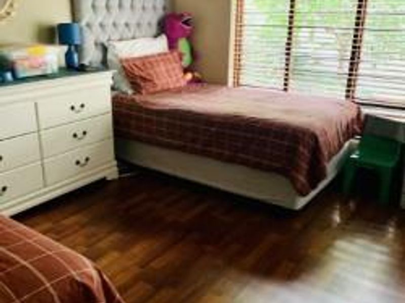 A bedroom featuring laminate flooring and venetian blinds, providing a functional space with natural light.