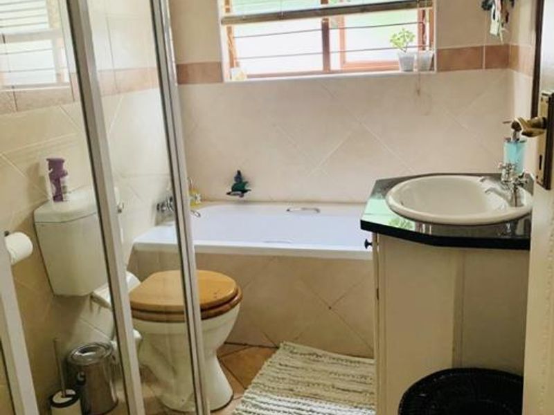 A functional bathroom featuring a shower enclosure, bathtub, toilet, and a vanity with a basin, finished with neutral wall and floor tiles.