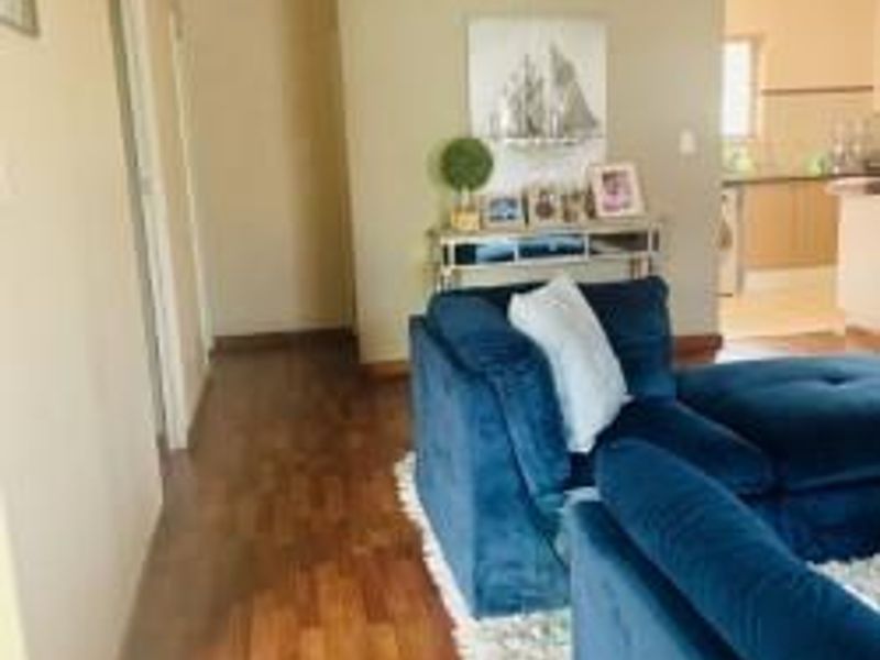 Open plan living area featuring warm-toned laminate flooring and coved ceilings, with a clear transition into the adjacent kitchen space.