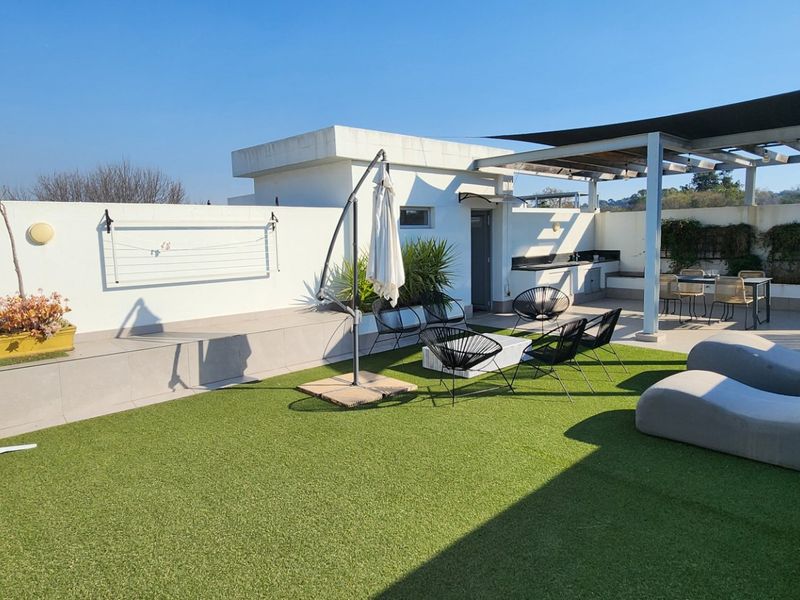 Spacious rooftop terrace featuring artificial grass, a built-in outdoor kitchen, and a shaded pergola area, perfect for outdoor entertaining.