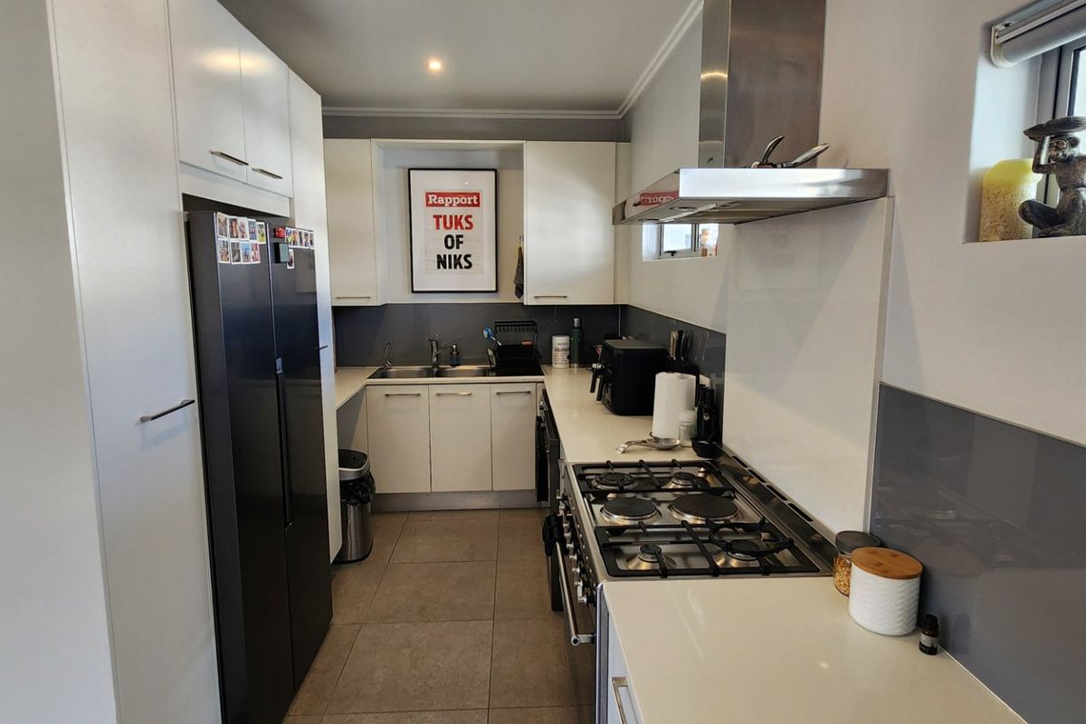 Modern galley-style kitchen featuring white cabinetry, stone countertops, a gas hob with extractor fan, and a sleek glass splashback.