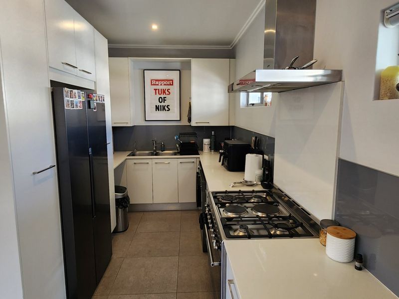 Modern galley-style kitchen featuring white cabinetry, stone countertops, a gas hob with extractor fan, and a sleek glass splashback.