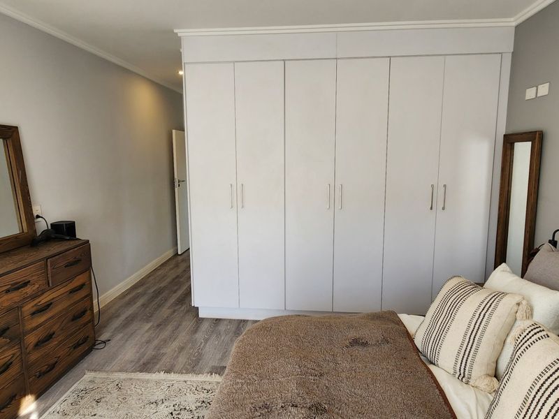A well-maintained bedroom featuring neutral walls, modern laminate flooring, and extensive floor-to-ceiling built-in cupboards for ample storage.