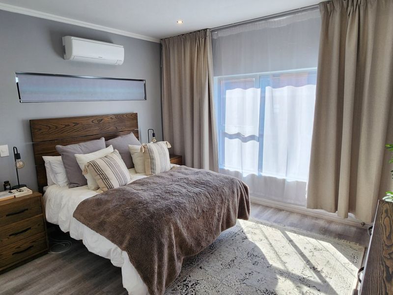 A well-maintained bedroom featuring laminate flooring, recessed lighting, and a wall-mounted air conditioning unit, offering a comfortable and modern living space.